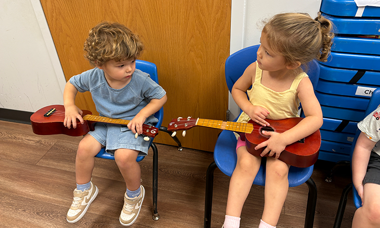 Students-hold-guitars Two students hold guitars while sitting in chairs side-by-side