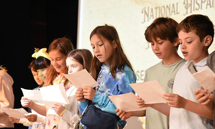 Assembly Doherty students stand up on stage, reciting a song in Spanish